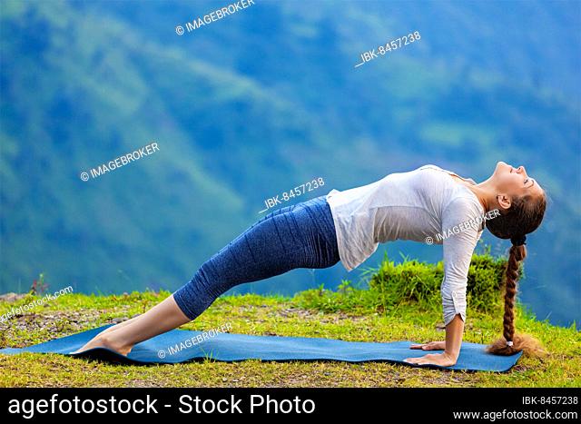 Woman doing Hatha yoga asana Purvottanasana plank pose outdoors in mountains