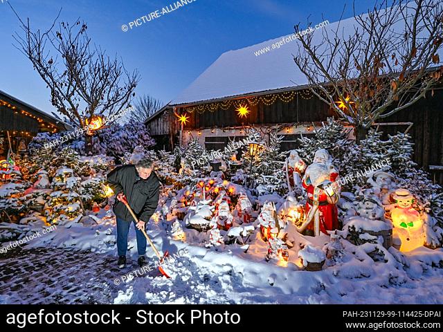 28 November 2023, Brandenburg, Straupitz: Gerd Mörl shovels snow in his festively decorated garden. He and his wife Gisela Liebsch collect Christmas figurines