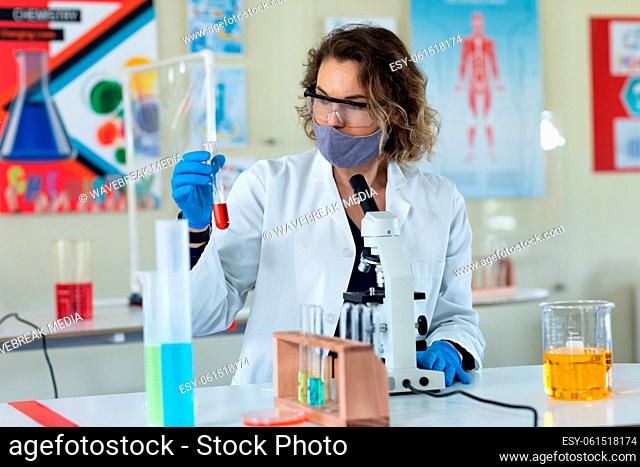 Female teacher wearing face mask and protective glasses holding a test tube in laboratory