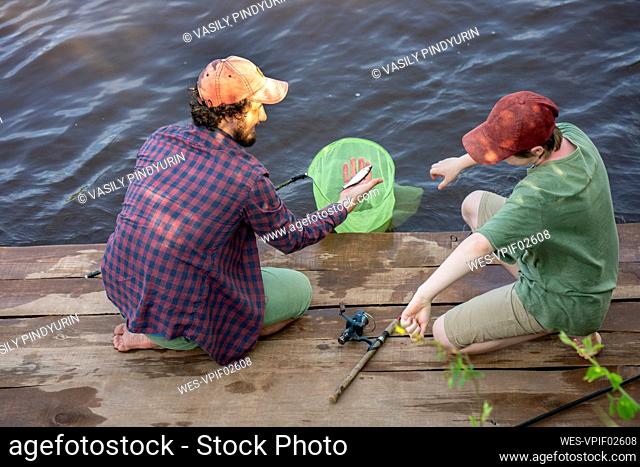 Father and son with catch of fish on boardwalk at riverbank