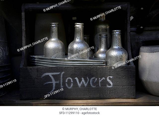 An old wooden basket with a label filled with silver-painted bottles