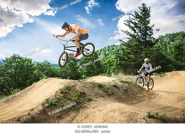 Two male friends riding BMX and mountain bikes on rural pump track