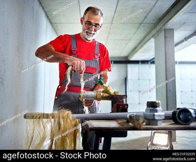 Plumber tying hemp gasket to metal pipe at workbench