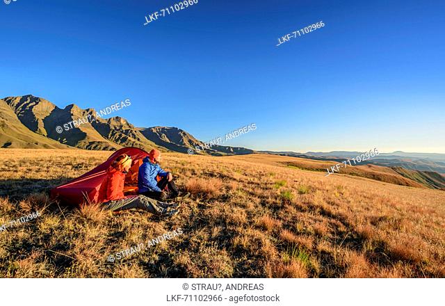 Woman and man sitting in front of tent, mountains above Giant's Castle in background, Giant's Castle, Drakensberg, uKhahlamba-Drakensberg Park