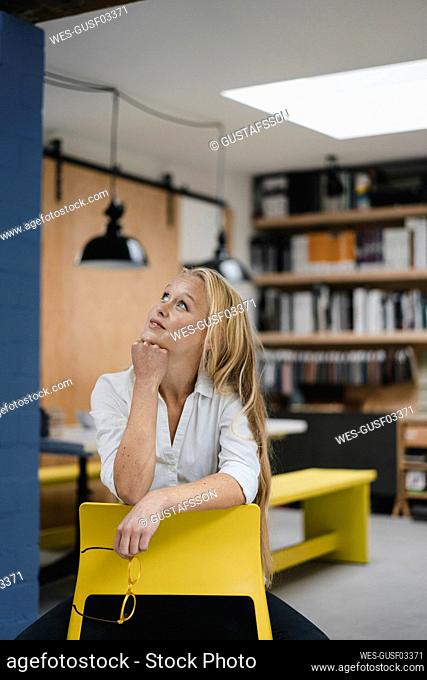 Smiling young businesswoman sitting on a chair in loft office looking up