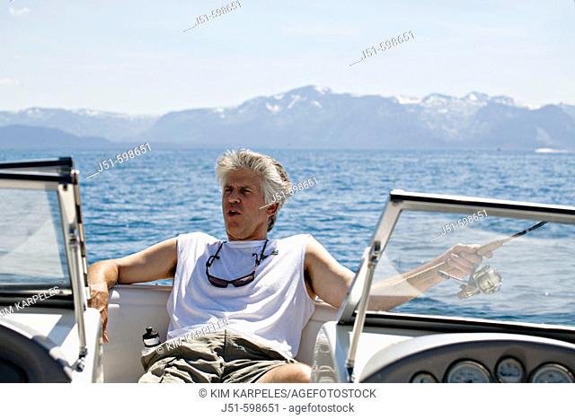 CALIFORNIA   Lake Tahoe   Adult male in sleeveless shirt relax on motor boat, sunglasses around neck, hold fishing rod in hand