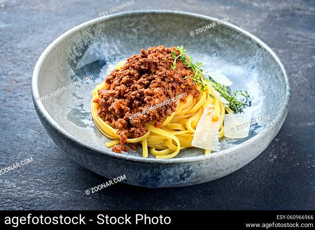 Modern style traditional Italian ragu alla bolognese sauce with linguine pasta noodles and parmesan cheese served as close-up in a ceramic design bowl with copy...