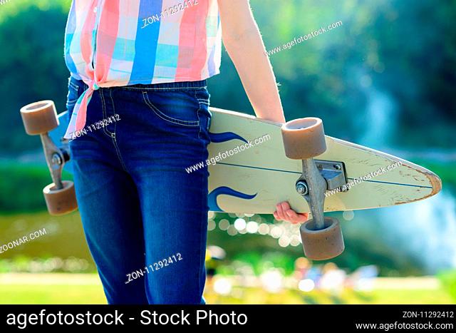 Young skateboard girl holding her longboard outdoors on sunset. Hipster girl with skateboard