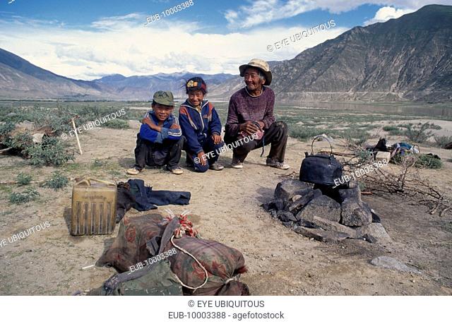 Shepherd and family crouching by camp in open landscape
