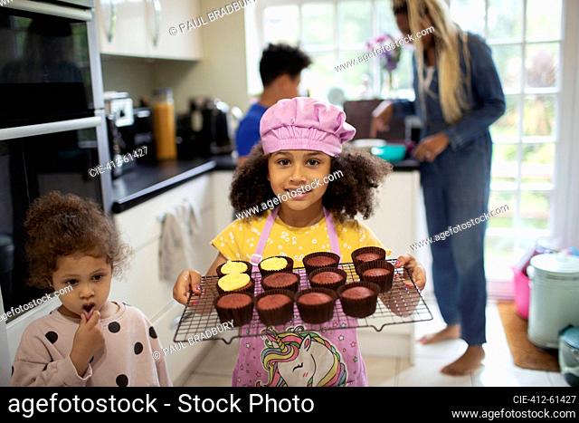 Portrait cute girl holding rack of baked cupcakes in kitchen