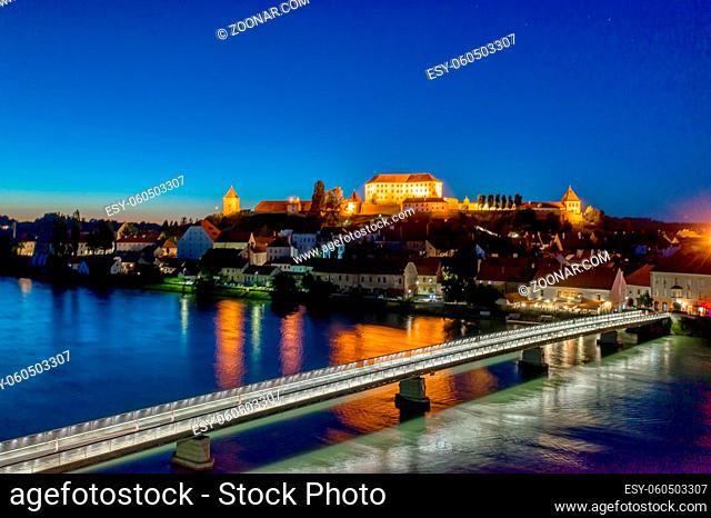 Panoramic view of Castle on top of hill at night, aerial view of Ptuj, Slovenia in dusk with illuminated foot bridge across the Drava river