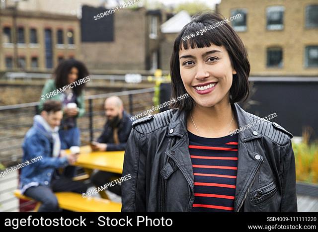 Portrait of Woman with group of friends working on tablets at outdoor patio table in co-working space in the background