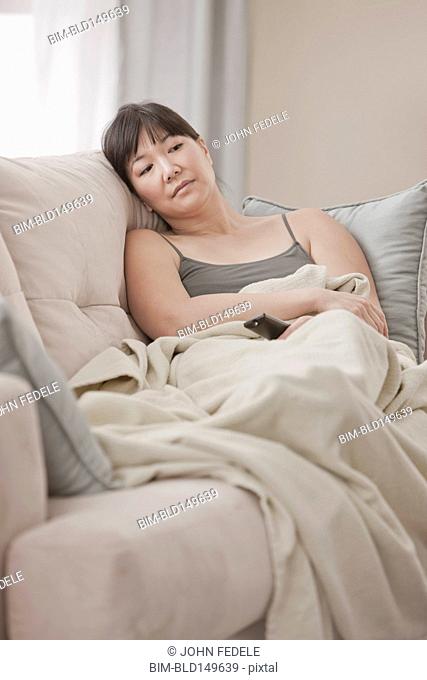 Asian woman laying on sofa watching television
