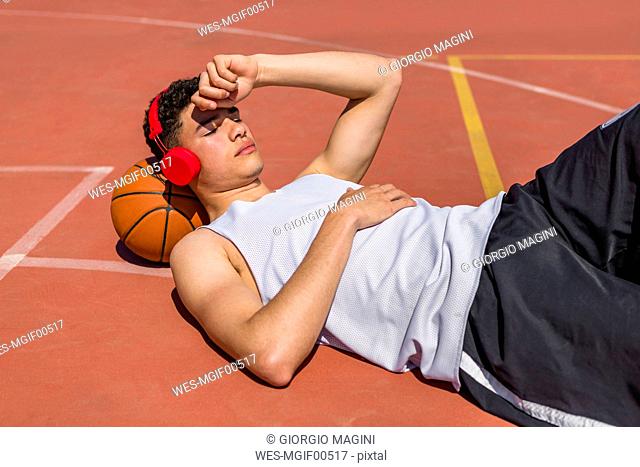 Young man lying on basketball, red headphones