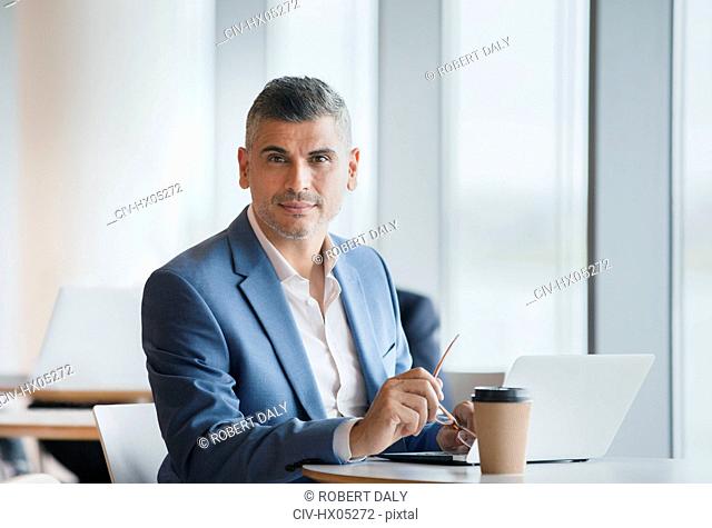 Portrait confident businessman working at laptop and drinking coffee