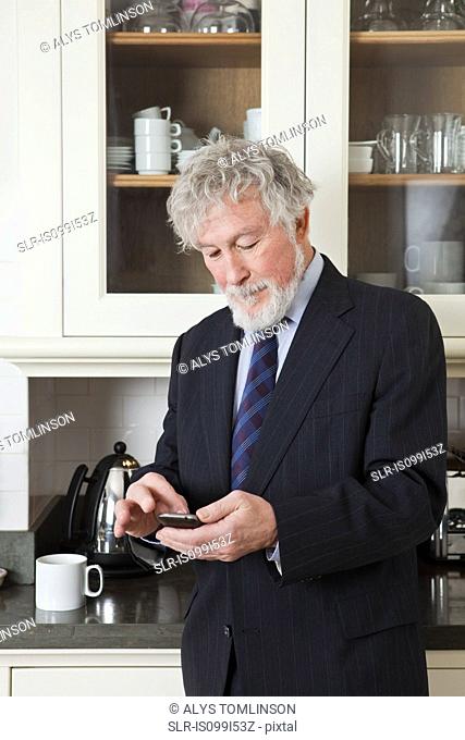 Senior businessman in kitchen with smartphone