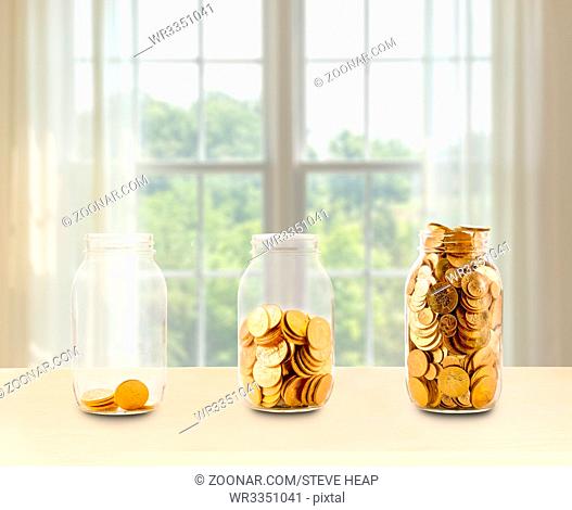 Concept of investment or savings for retirement with three glass jars filled with gold coins in front of bright window