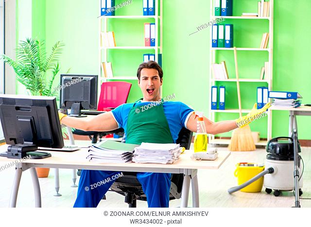 Handsome man cleaning office with vacuum cleaner
