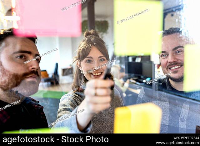 Happy businessmen and businesswoman discussing over adhesive notes in office