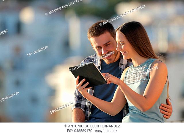 Happy couple browsing tablet content outside in a town outskirts at sunset