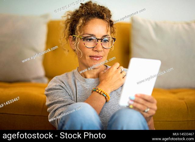 Happy relaxed adult cute woman use electronic device reader to read an e-book and enjoy her indoor leisure activity at home