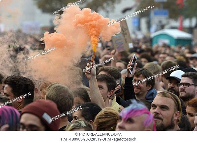 03.09.2018, Saxony, Chemnitz: A spectator with an orange smoke torch stands before the concert under the motto ""#we are more"" on the parking lot in front of...