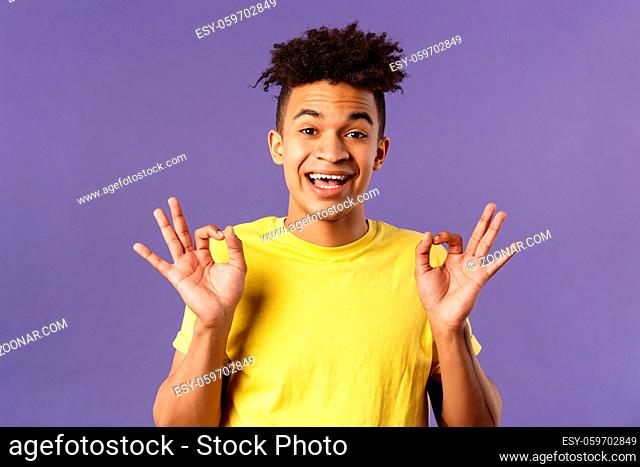 Close-up portrait of upbeat, relaxed young hipster guy with dreads assuring all good, everything be okay, show OK gesture and smiling