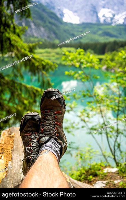 Italy, Province of Udine, Tarvisio, Feet of man wearing hiking boots relaxing on shore of Fusine Lake