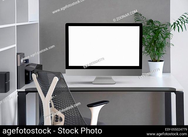 Daylight interior with white modern mock-up computer monitor on an office table, orthopaedic chair, and greenery pot on a desk, copy space