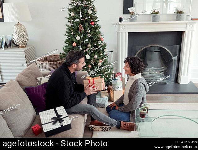 Husband giving Christmas gift to wife by tree in living room