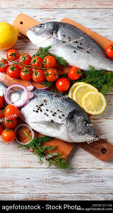 Raw fresh uncooked dorado or sea bream fish with lemon, herbs, cherry tomatoes and spices on black background