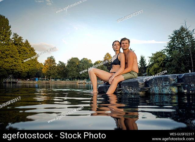 Young couple sitting on bathing platform on a lake looking at distance