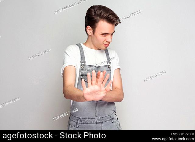 ?onfused young brunette man in casual style with white t-shirt and denim overalls standing, scared and asking to dont touch him and blocking