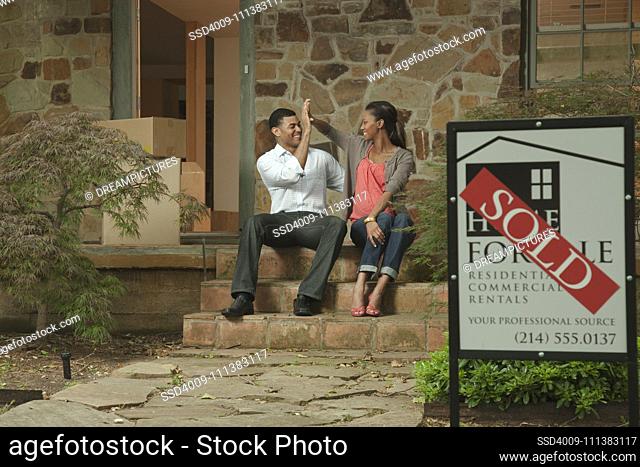 Couple sitting on front stoop of house with sold sign
