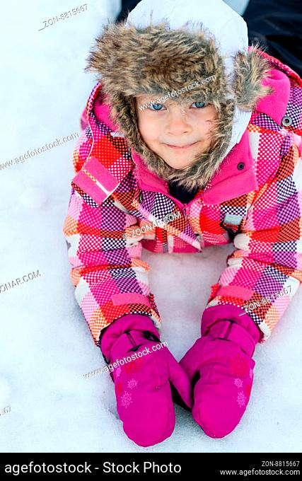 Little girl laying on snow - smiling child - winter fun