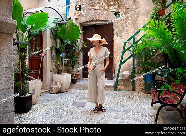Beautiful blonde young female traveler wearing straw sun hat sightseeing and enjoying summer vacation in an old traditional costal town at Adriatic cost