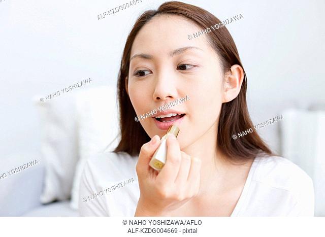 Young attractive Japanese woman doing her make-up at home