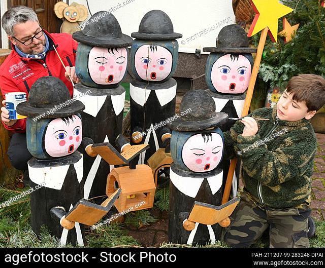 05 December 2021, Saxony, Borsdorf: Denny Pfaff (l) and his son Felix are repairing the chipped paint on the carol singers that decorate the Pfaff families'...