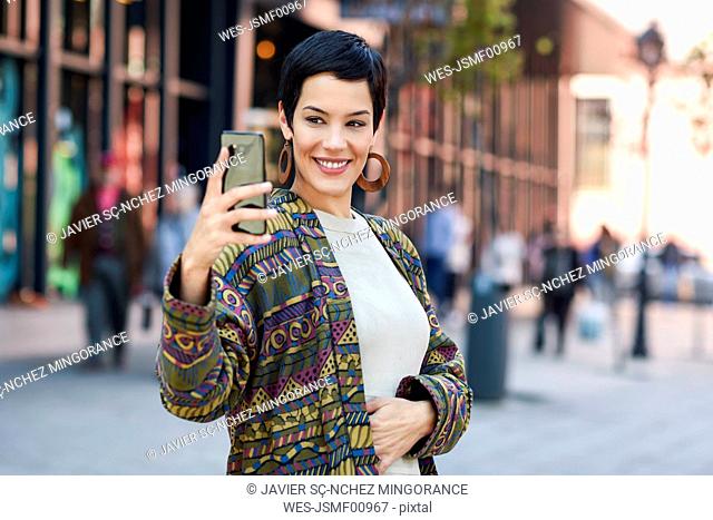 Smiling fashionable young woman taking a selfie in the city