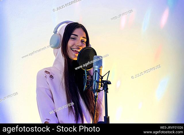 Smiling female singer wearing hooded top singing at studio