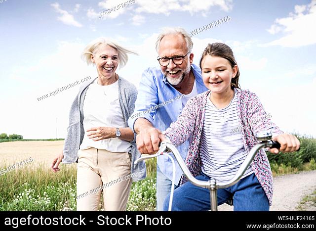 Smiling grandparents playing with granddaughter riding bicycle