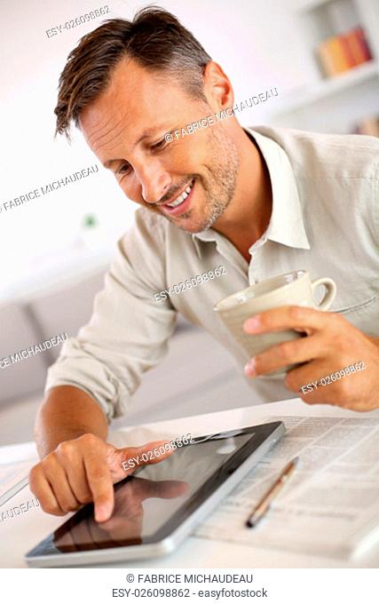 Man reading news on tablet and drinking coffee