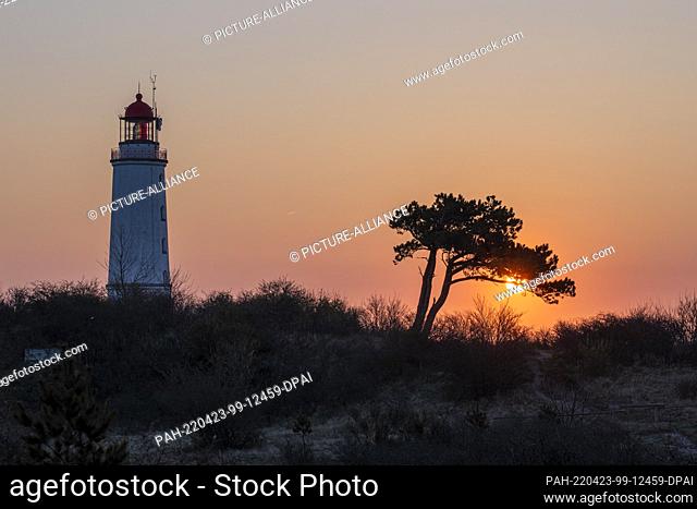 23 April 2022, Mecklenburg-Western Pomerania, Hiddensee: At the Dornbusch lighthouse on the Schluckwieksberg, the sky shows red pastel colors in the early...