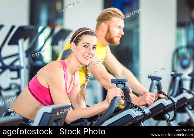 Portrait of a beautiful fit woman smiling while wearing pink fitness bra during routine on stationary bicycle at the gym