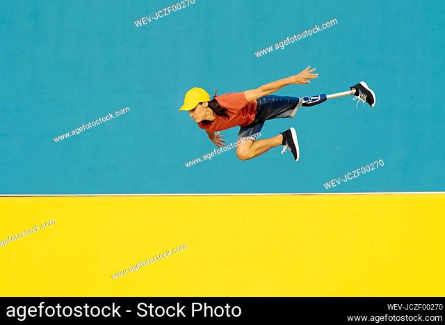 Athlete with artificial limb and foot jumping against multi colored wall