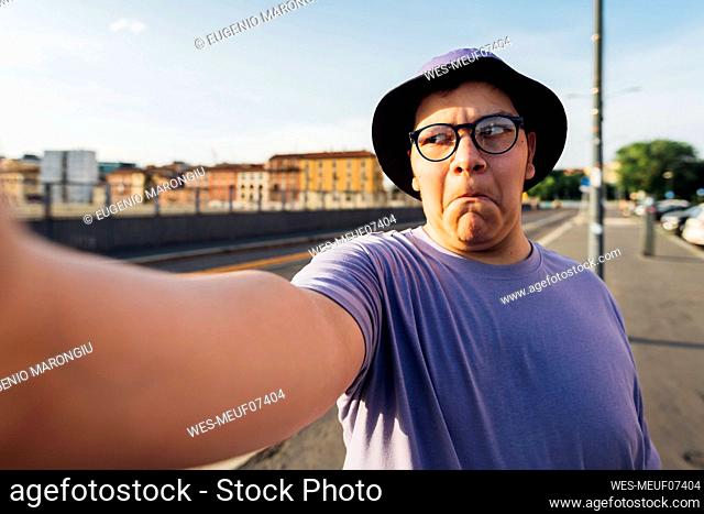 Teenage boy making face taking selfie on street