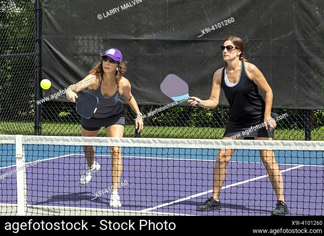 Two pickleball players in action at the net on a suburban pickleball court during summer