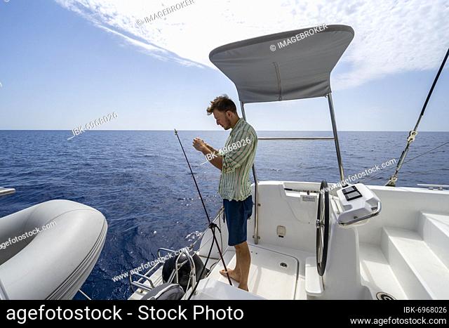 Young man fishing on a boat, sailing catamaran, sailing trip, Dodecanese, Greece, Europe