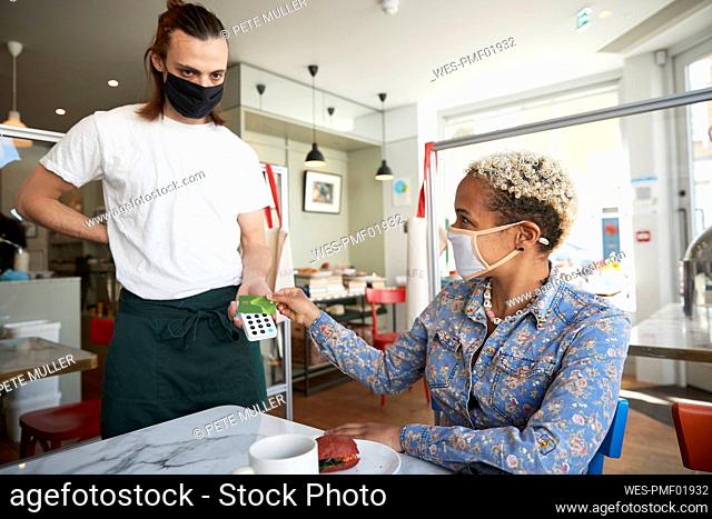 Mid adult woman making contactless payment in cafe during COVID-19