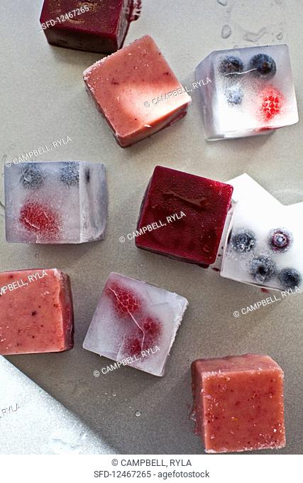 Smoothie ice cubes and ice cubes with berries on a metallic baking sheet